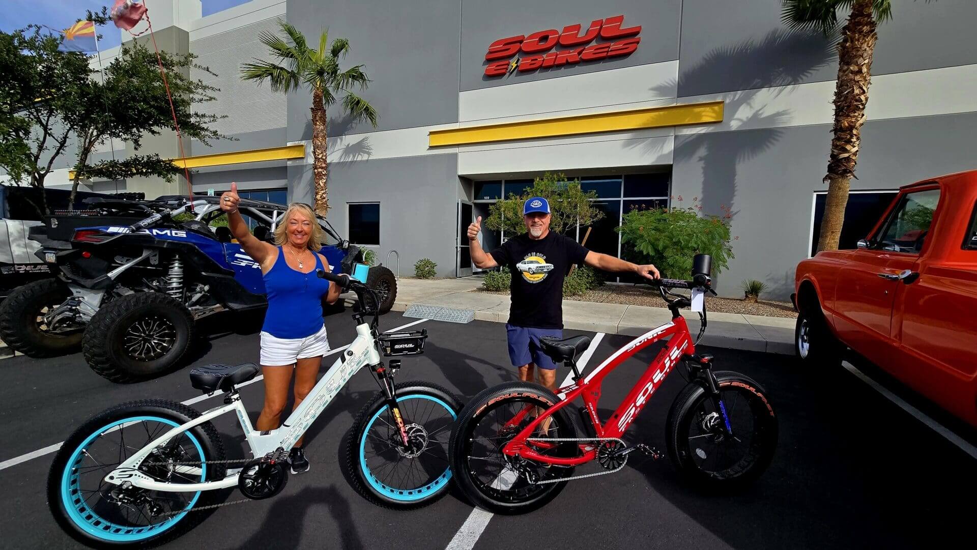 Two people with electric bikes outside store.