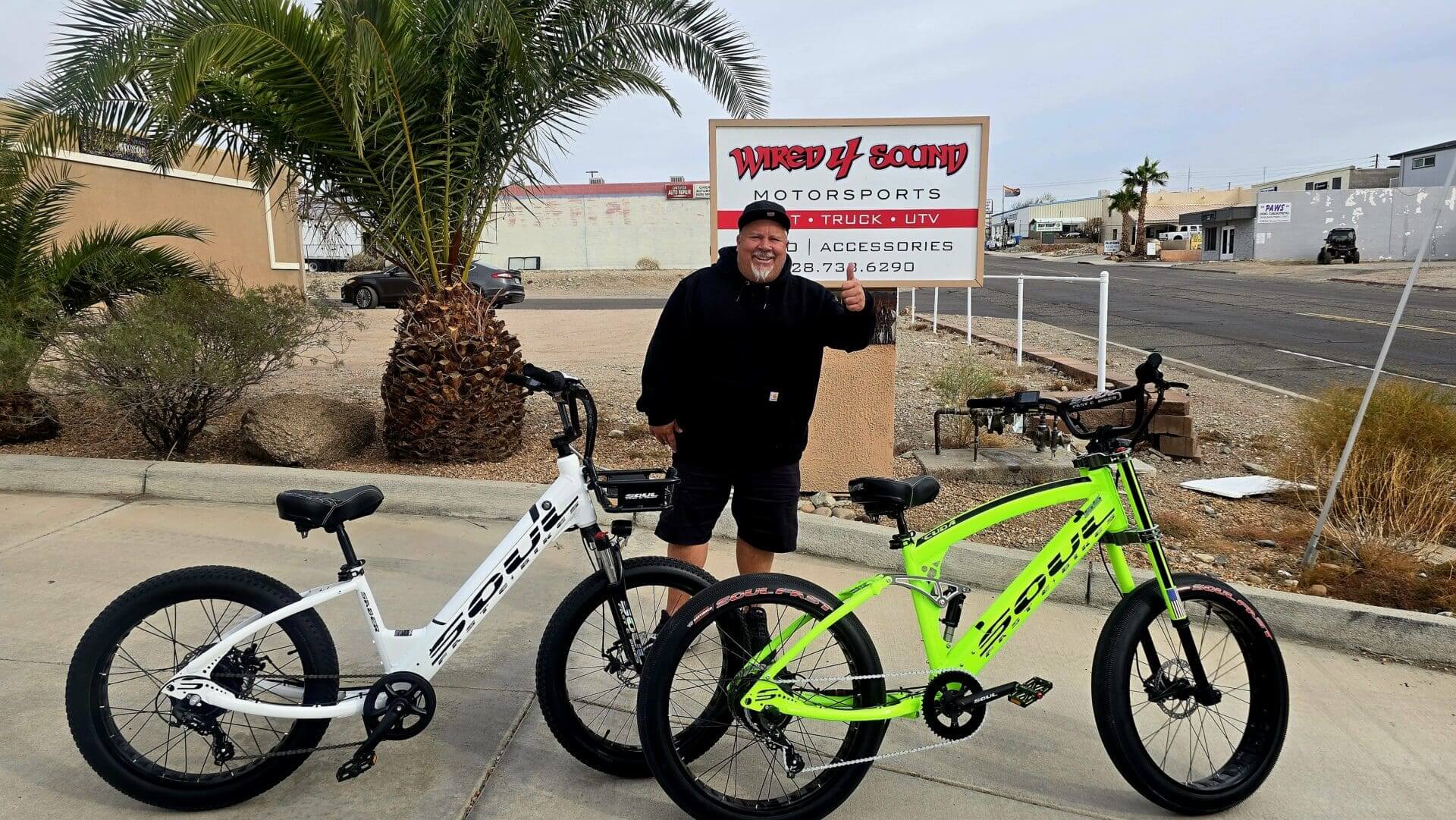 Man with two bicycles outside shop.