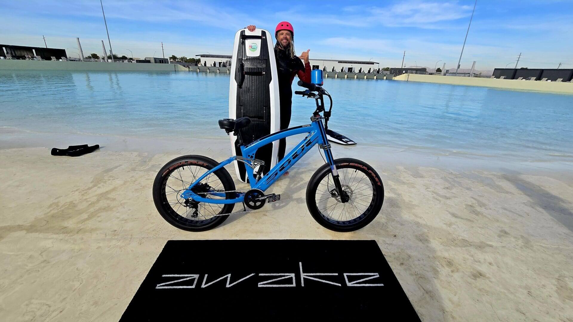 Blue bike and surfboard near water's edge.