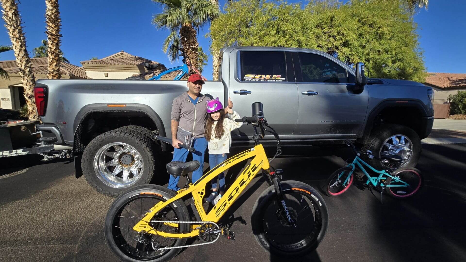 Man, child, bikes, and truck under palm trees.
