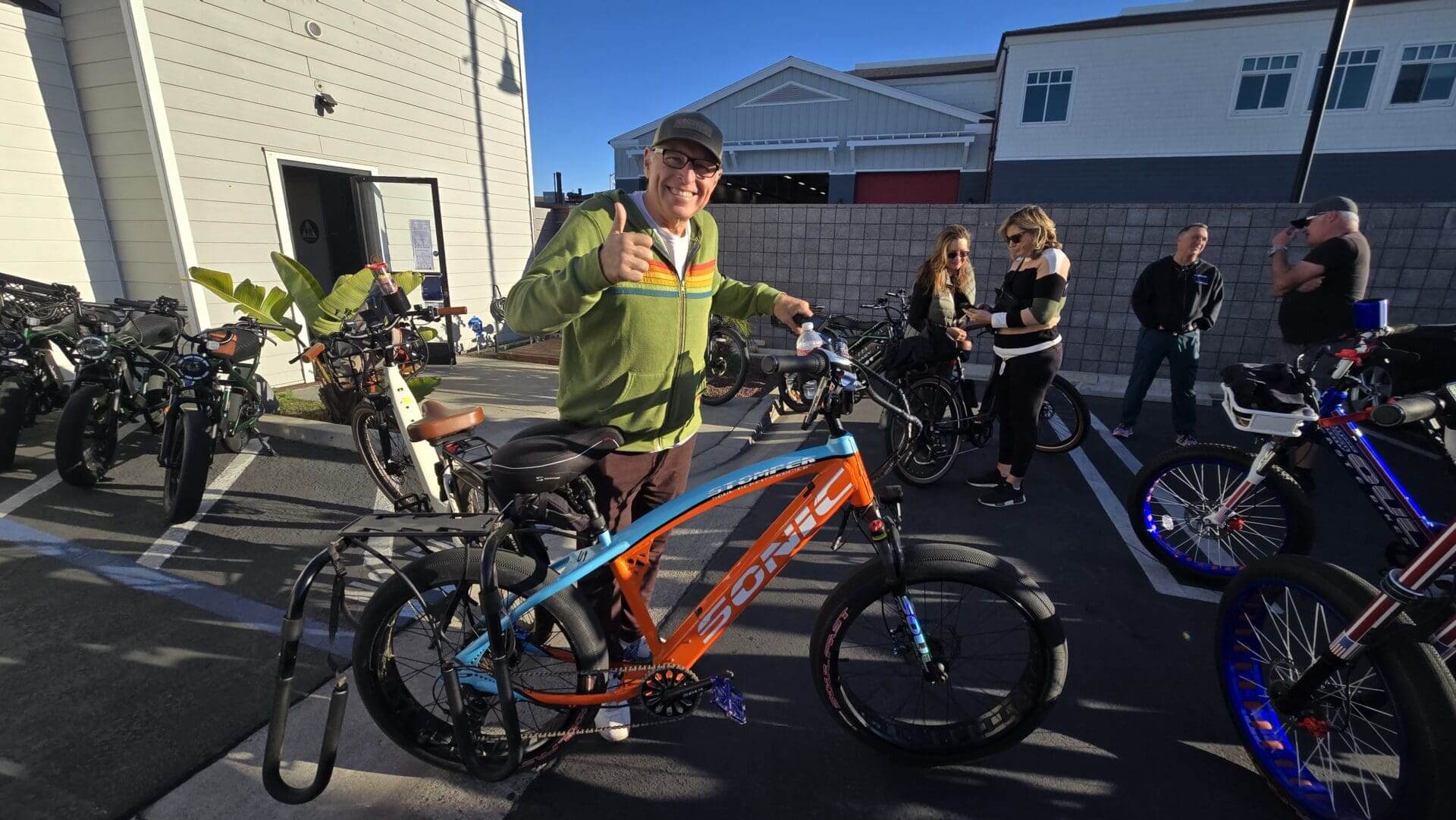 Man with orange bike, thumbs up, outdoors.