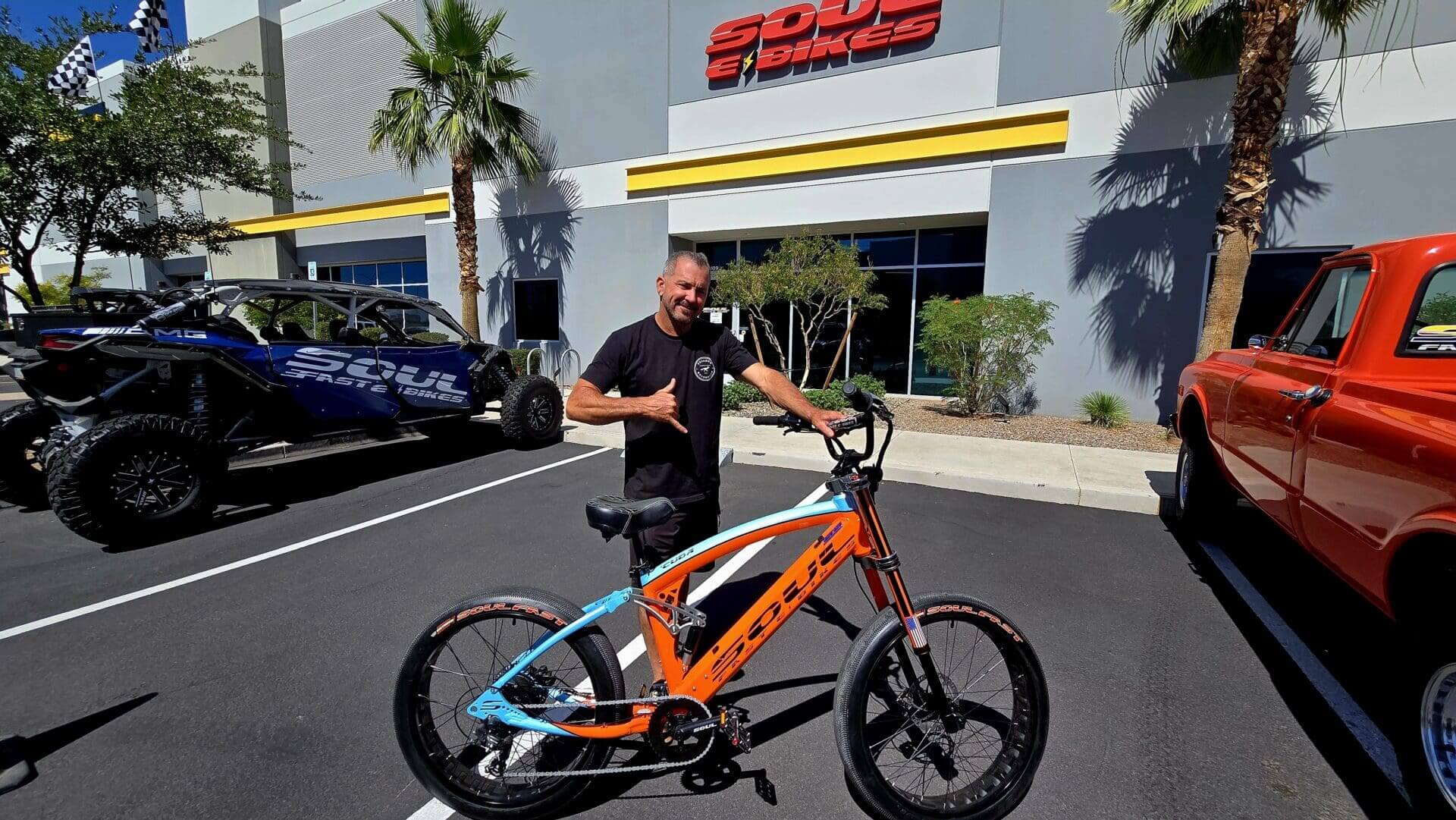Man posing with orange and blue bike.