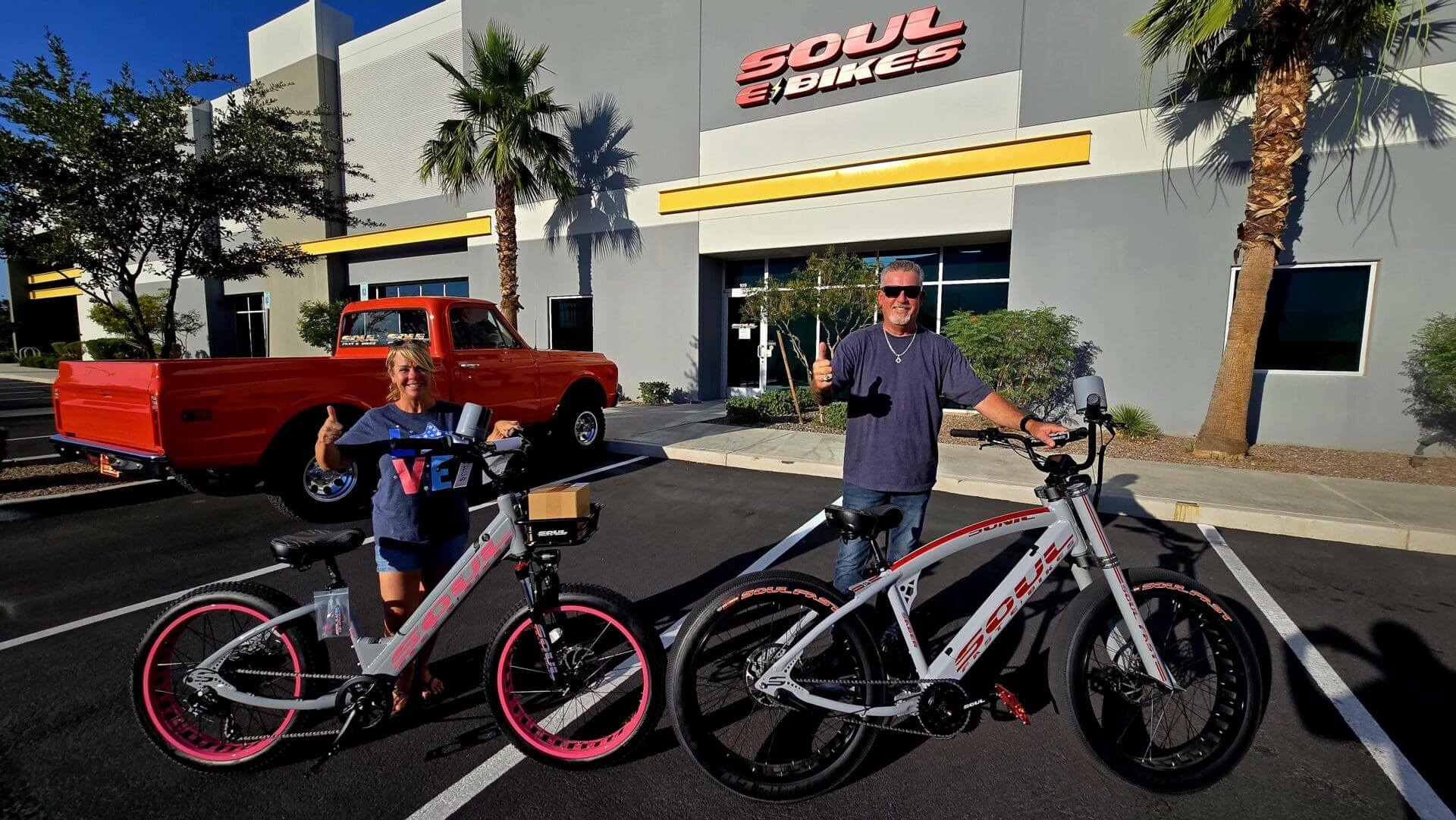 Two people with electric bikes outside shop.