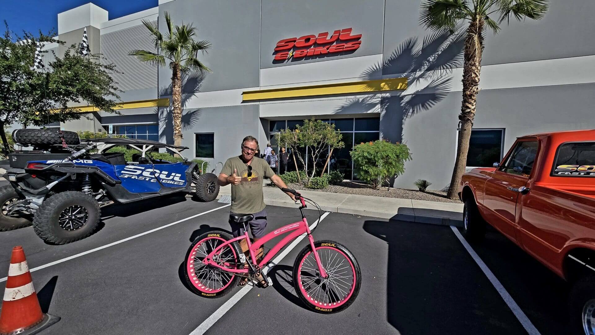 Man with pink bicycle outside store.
