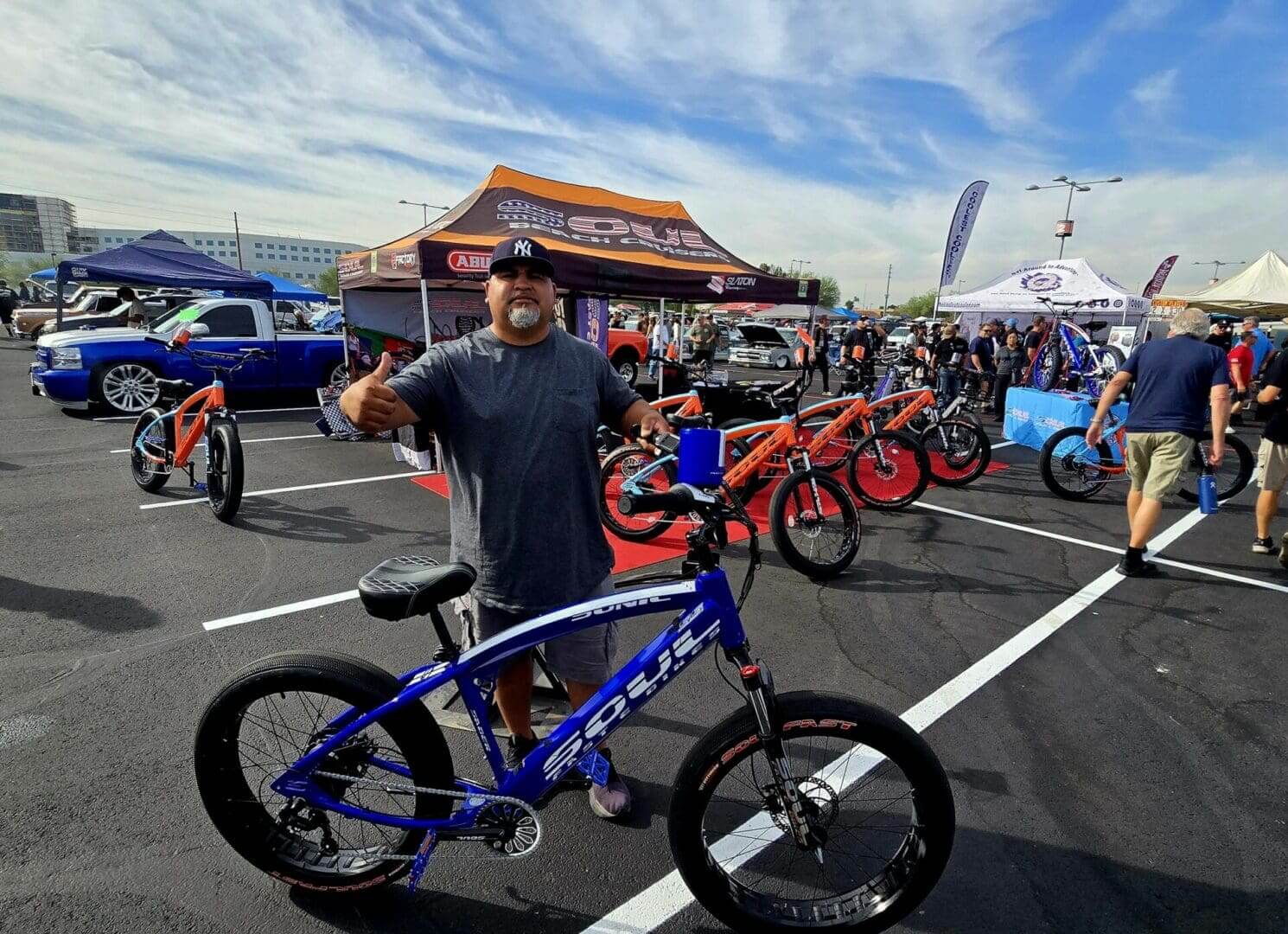Man posing with blue bicycle at event.