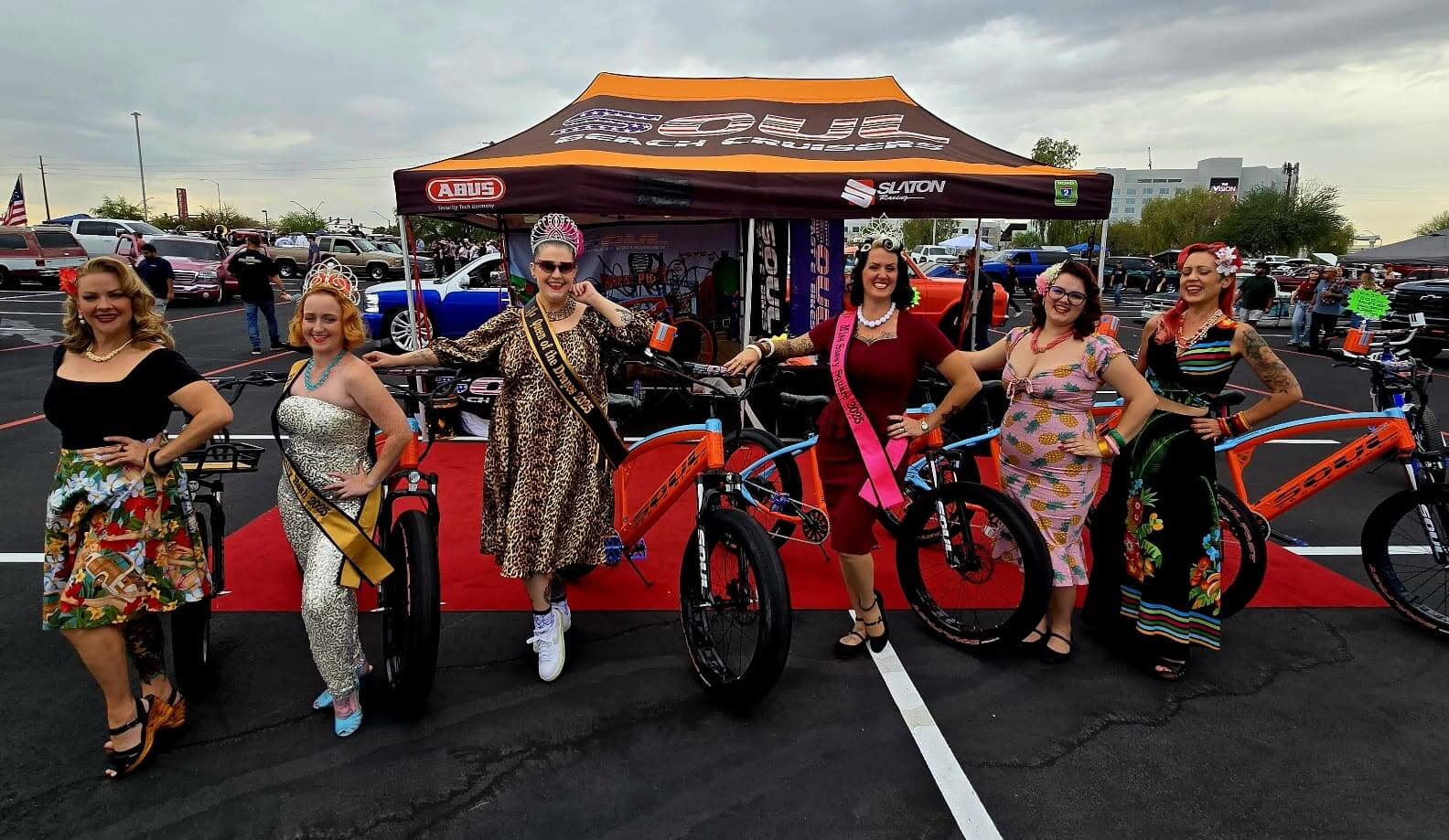 Women posing with bicycles at outdoor event.