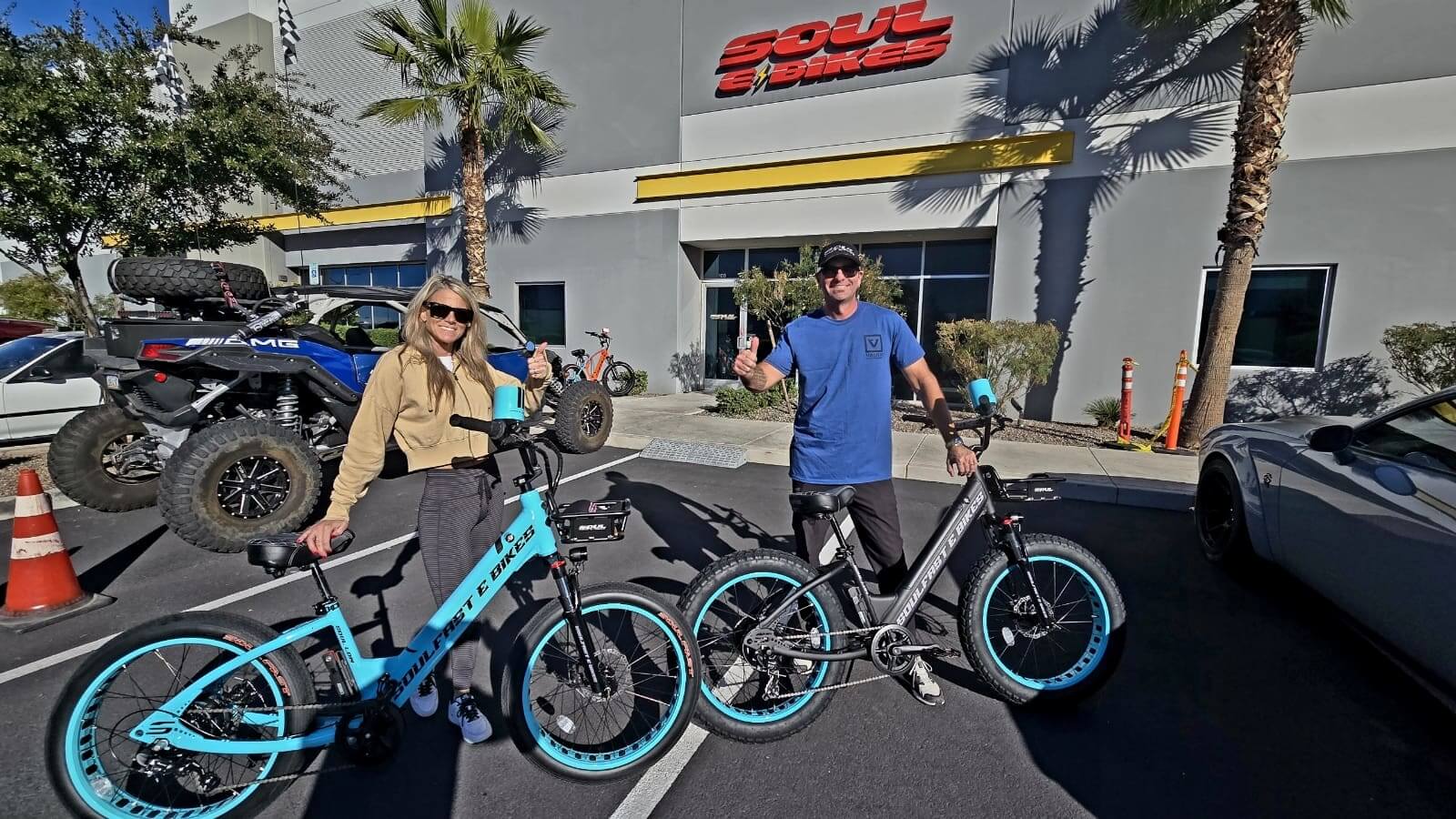 Two people with electric bikes outside shop.