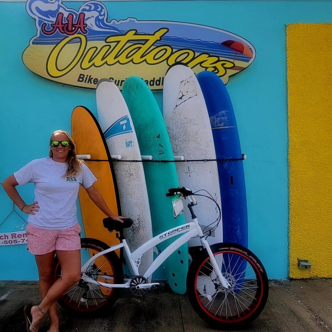 Woman with bike and surfboards outside shop.