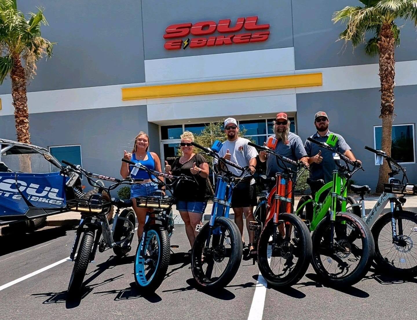Group with colorful electric bikes outside store.