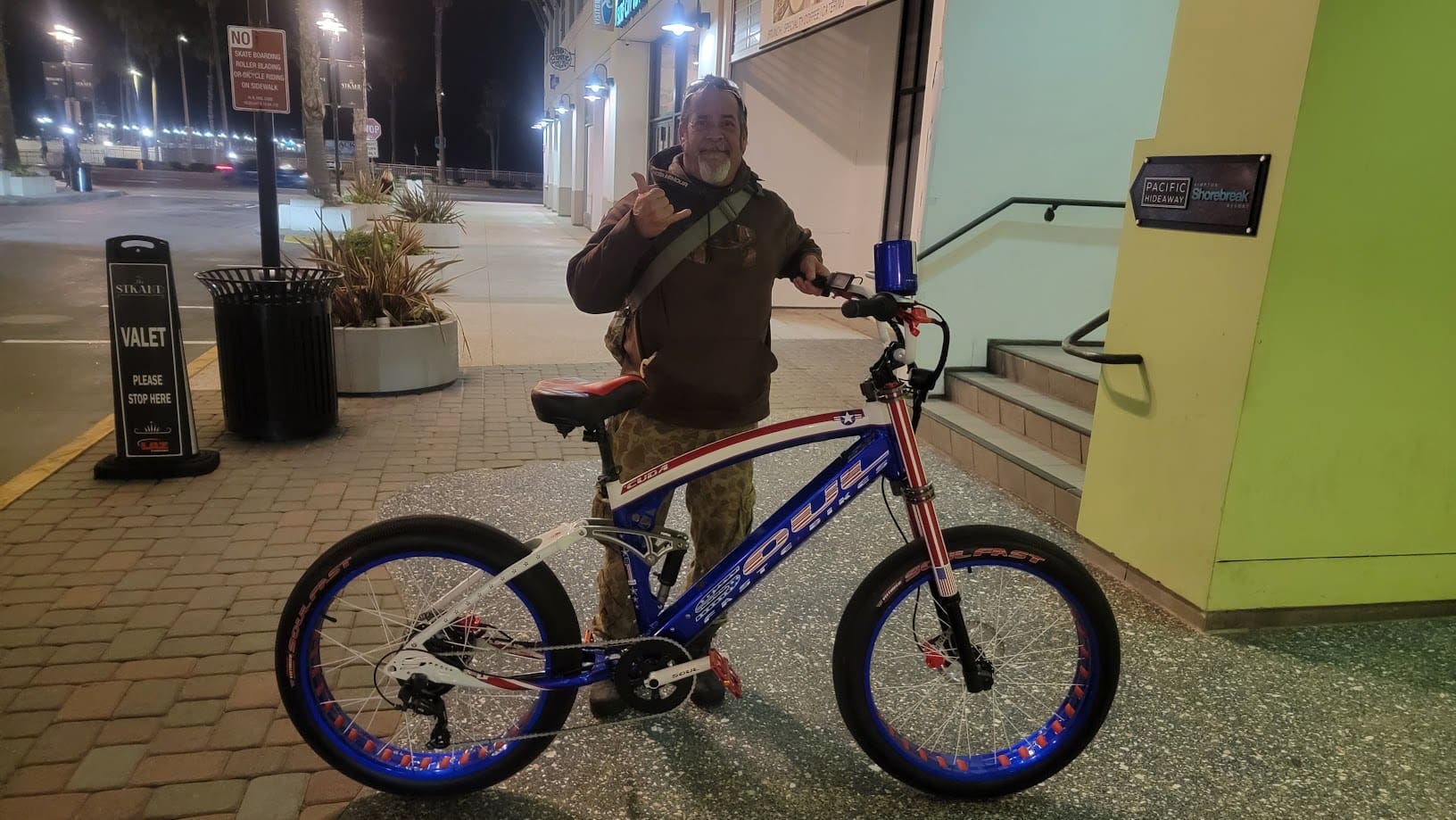 Man posing with bicycle on city sidewalk.