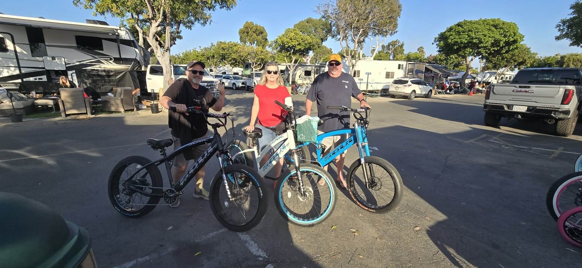 Three people with bicycles in parking lot.