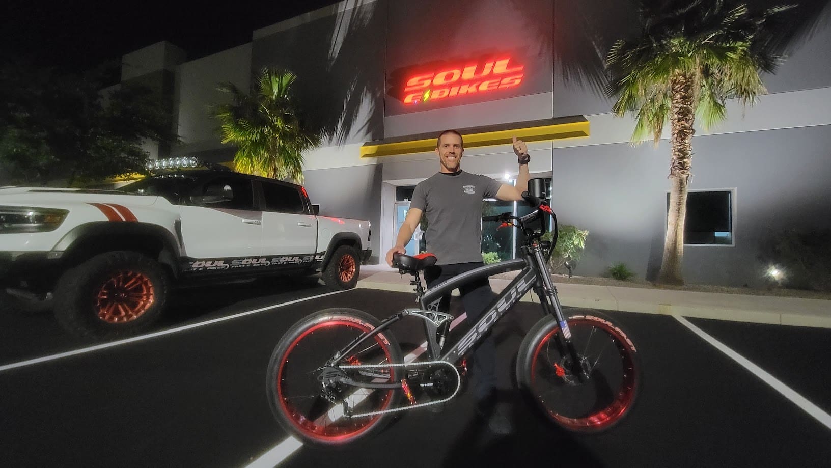 Man with bicycle outside illuminated building at night.