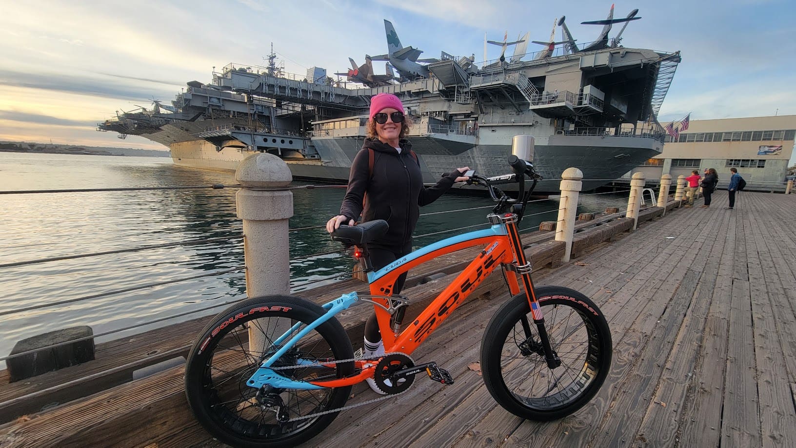 Person with bicycle near aircraft carrier ships.