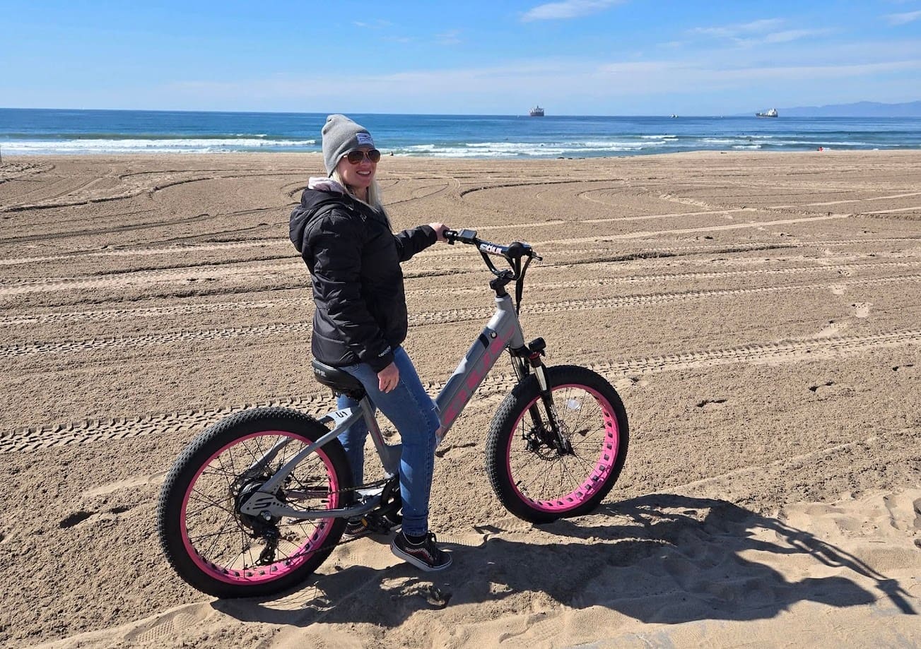 Person biking on sandy beach near ocean.