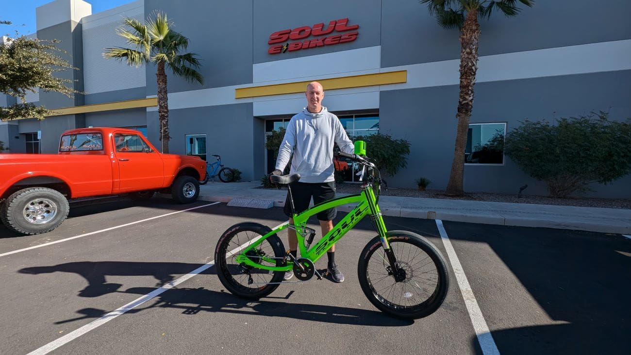 Person standing with a green bicycle outside.
