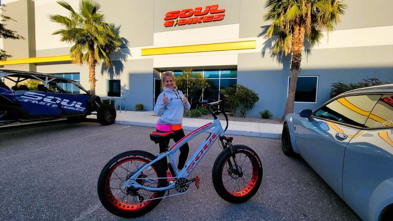 Woman posing with electric bike outside store.