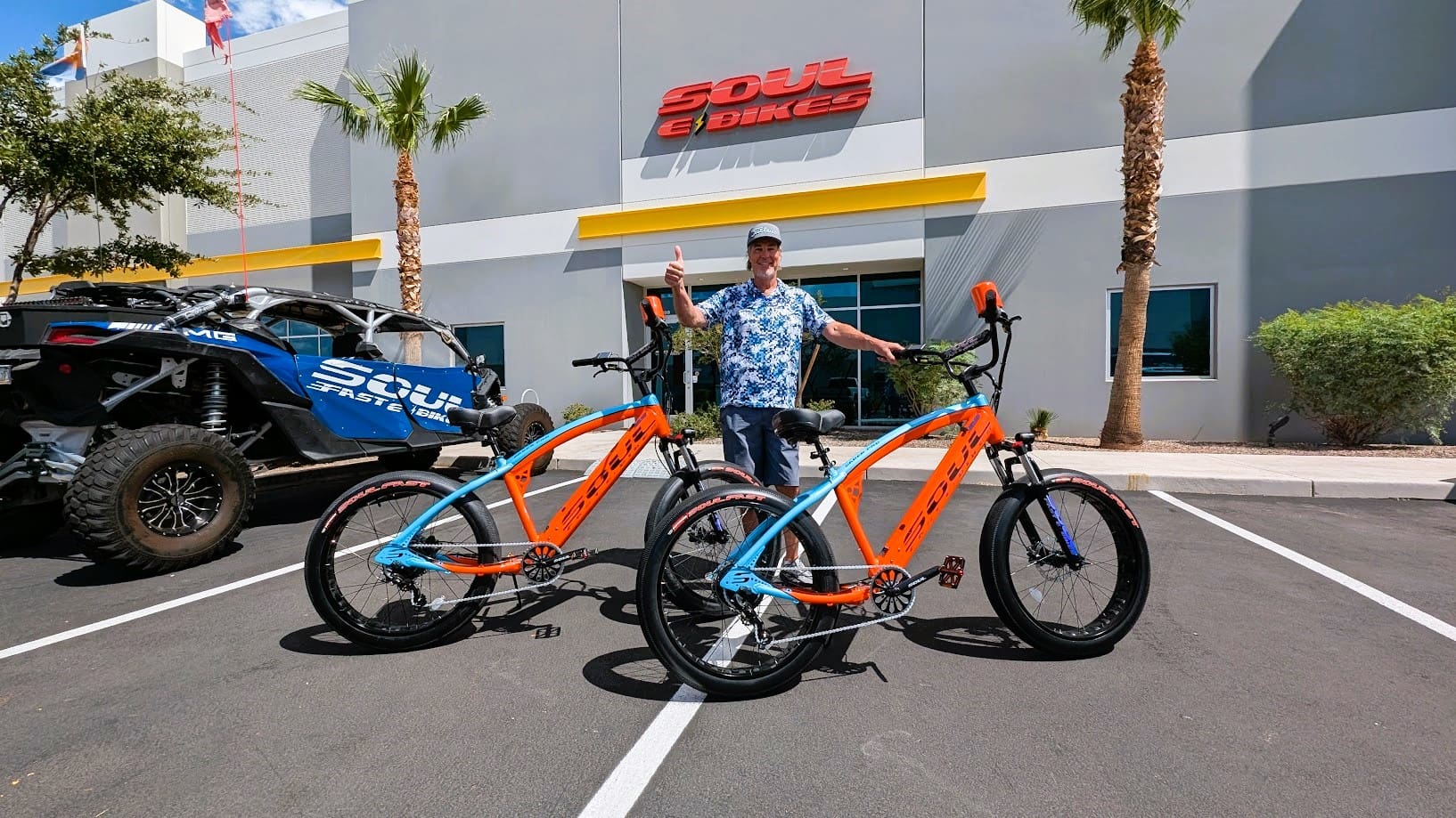 Man posing with two electric bikes outside.