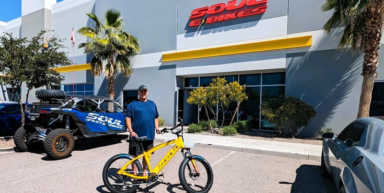 Man posing with yellow bike outside store.