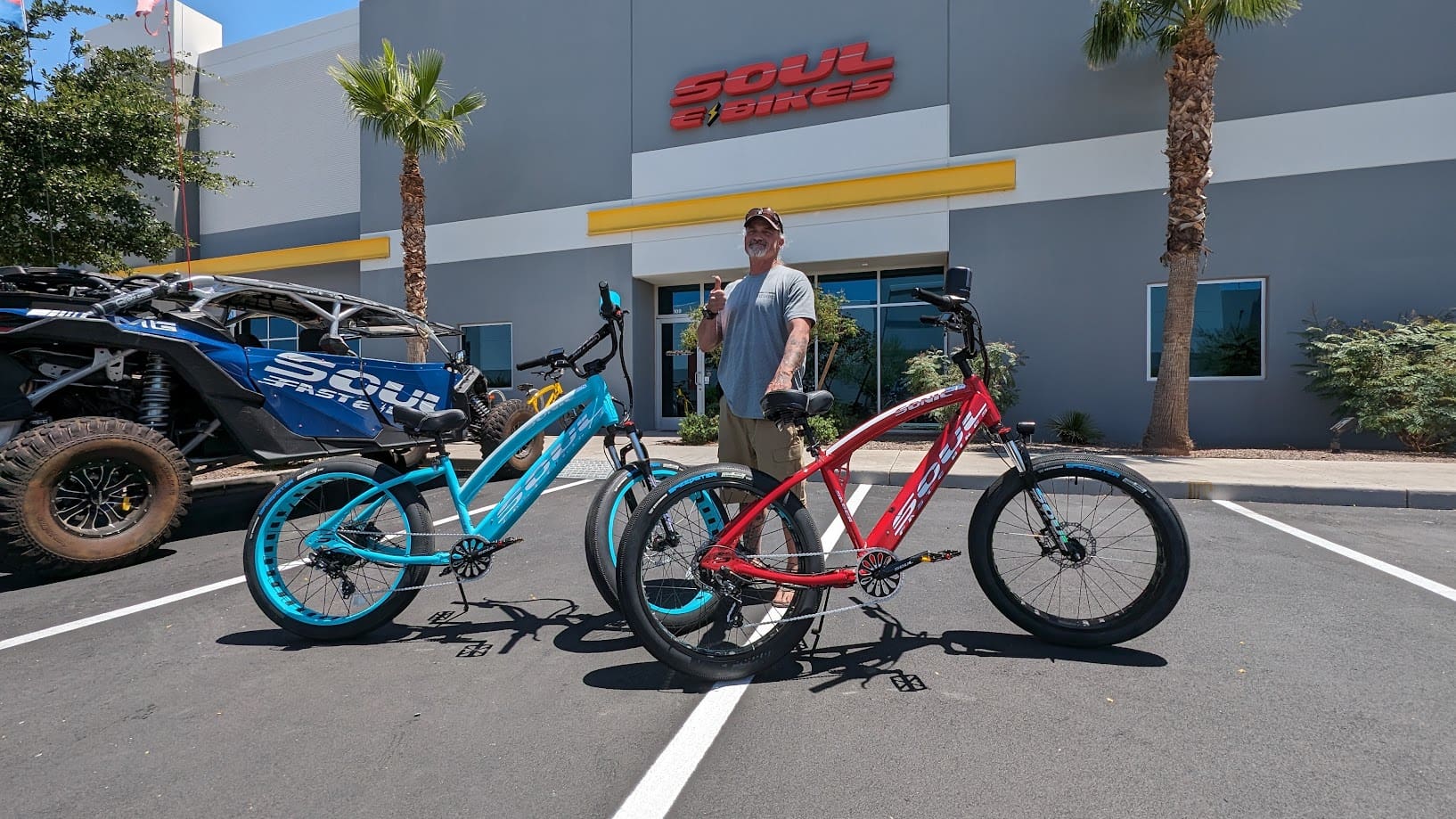 Man standing with two electric bicycles outside.
