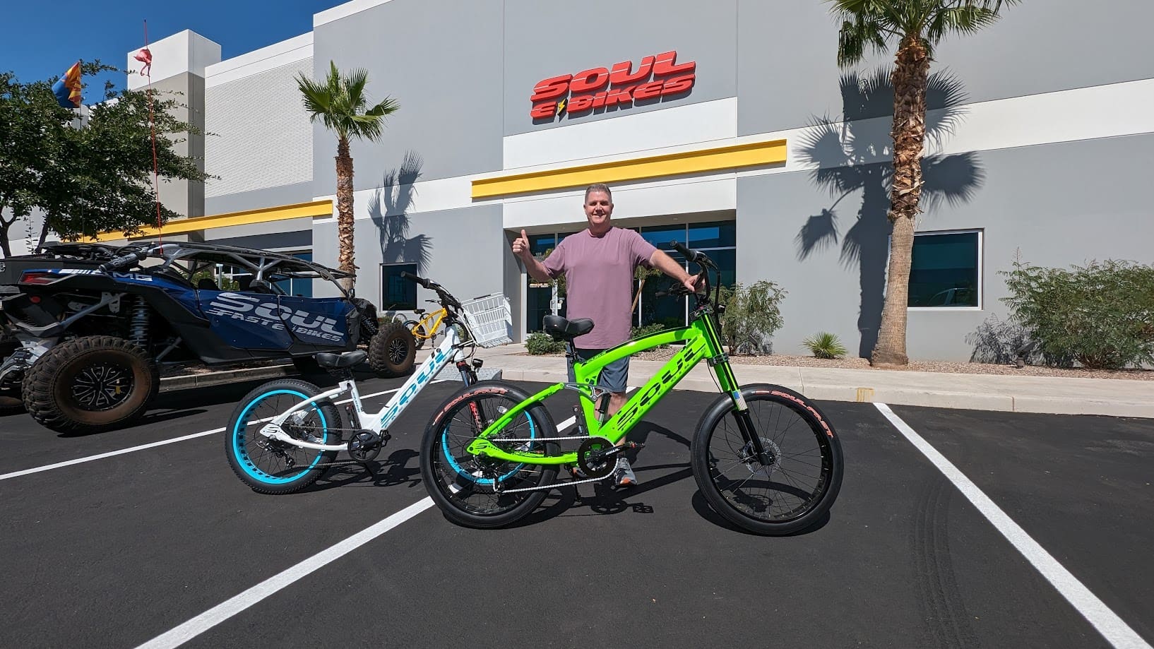 Man posing with two electric bikes outside.