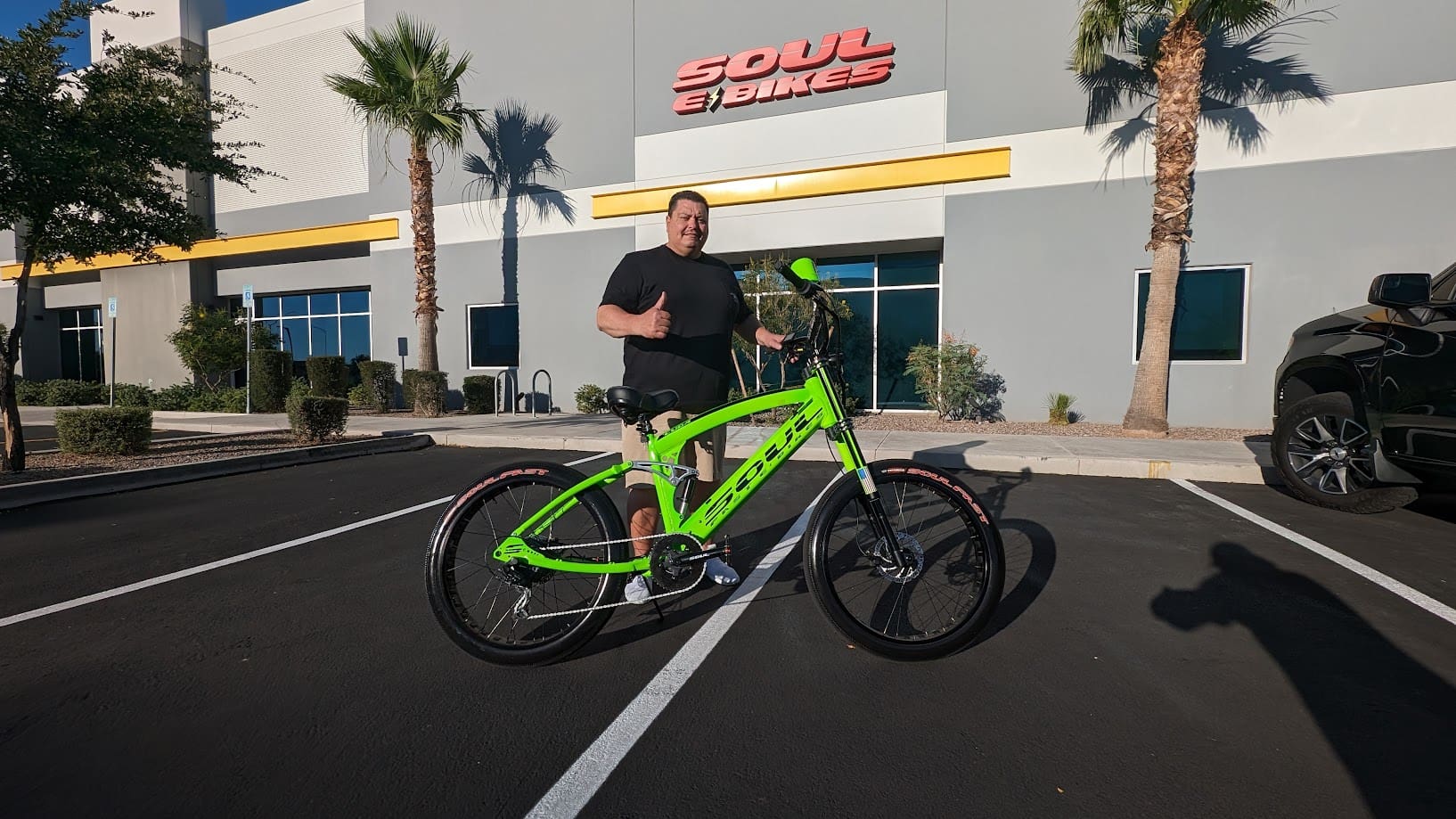 Man posing with green bike in parking lot.