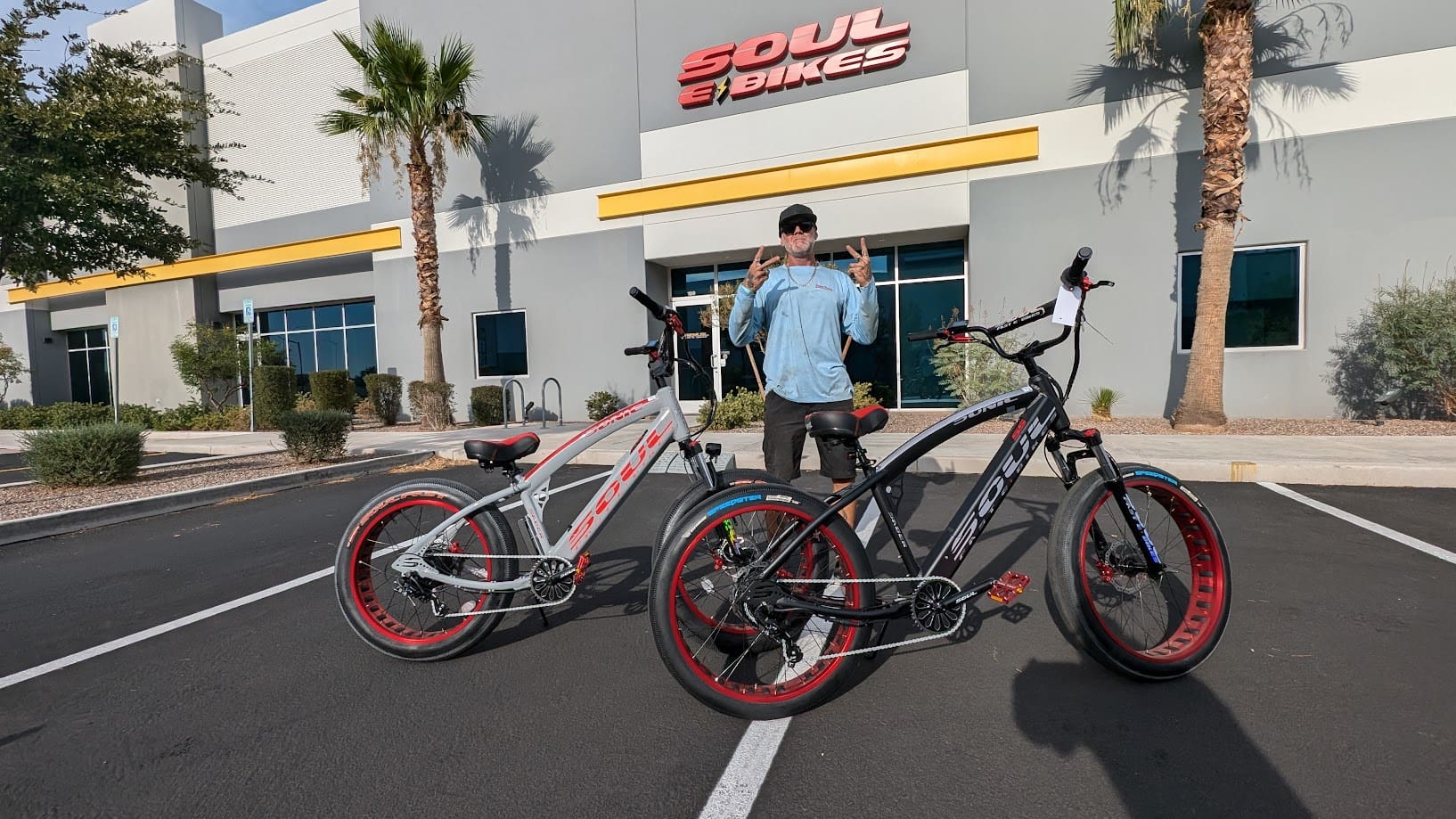 Man with two electric bikes outside store.