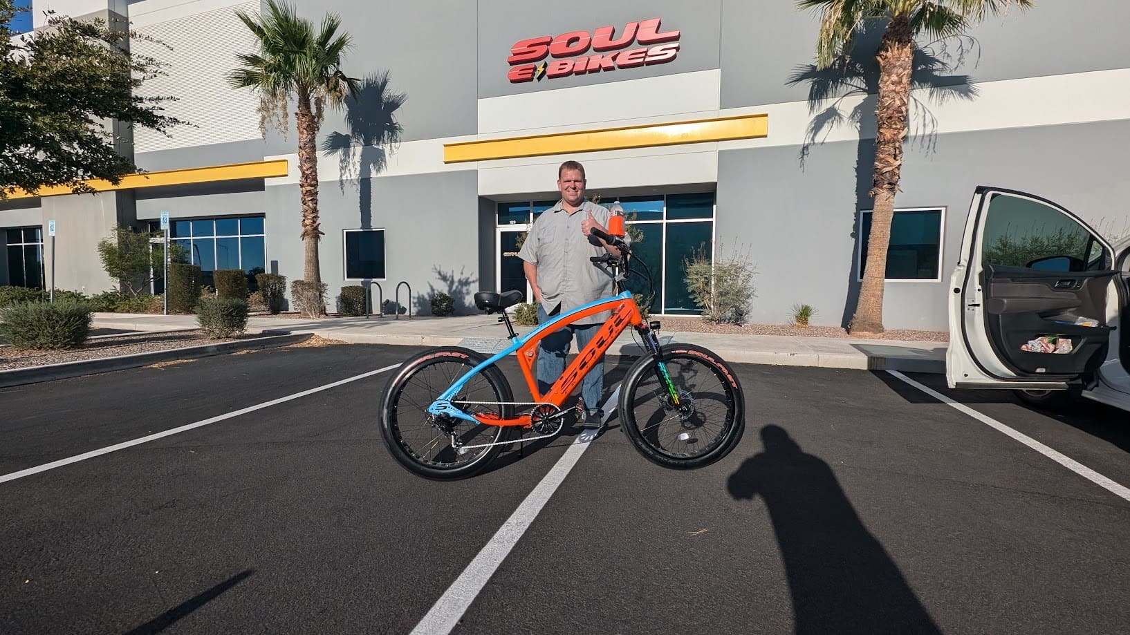 Man standing with colorful bike outside shop.