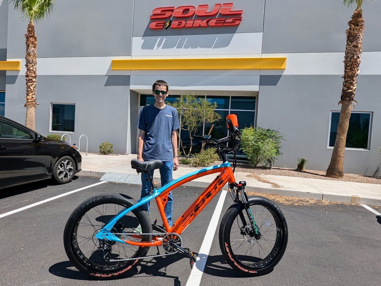 Person standing with an orange bicycle outside.
