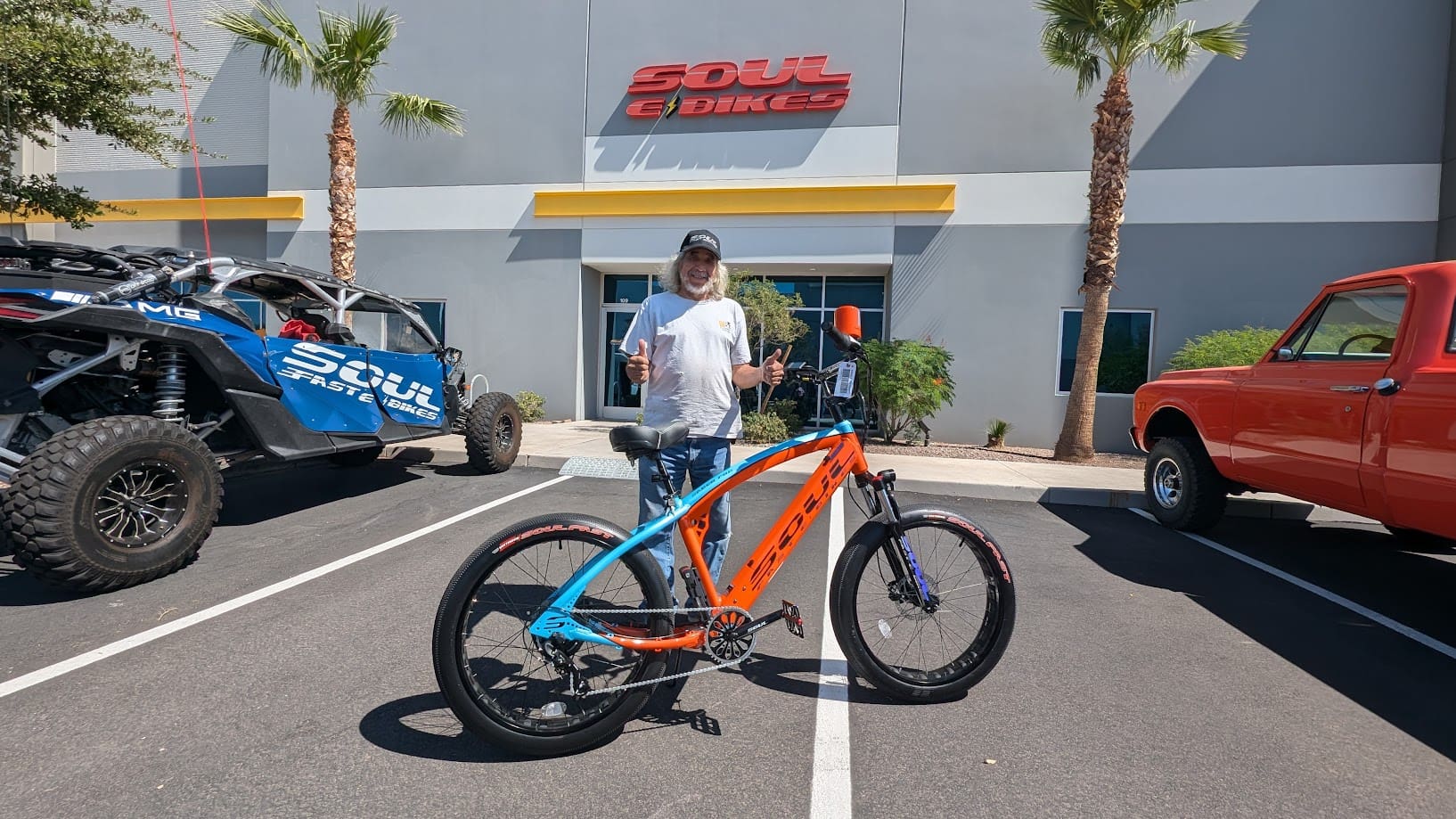 Man standing with orange-blue bicycle outside shop.