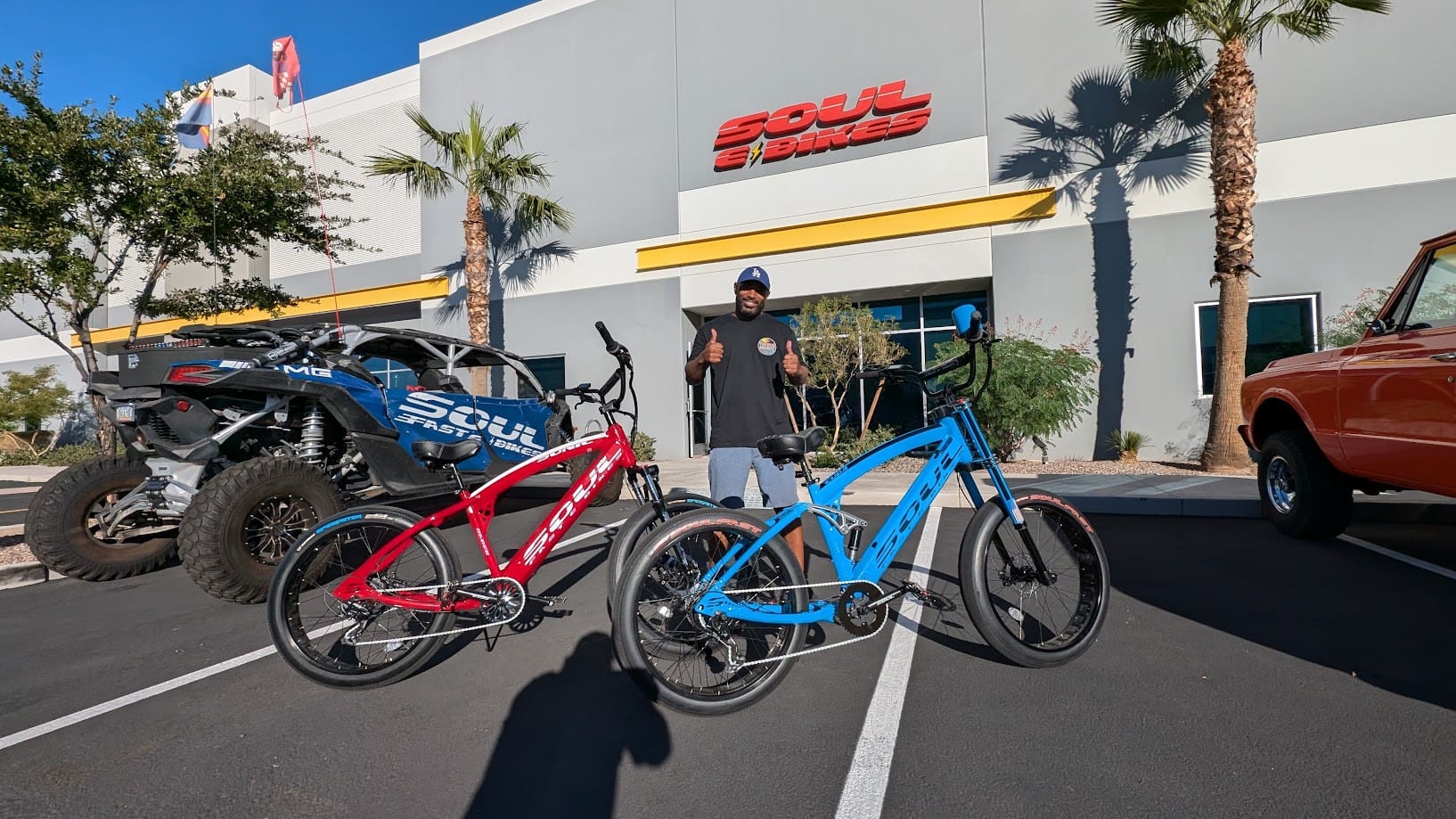 Man posing with two colorful bicycles outside.