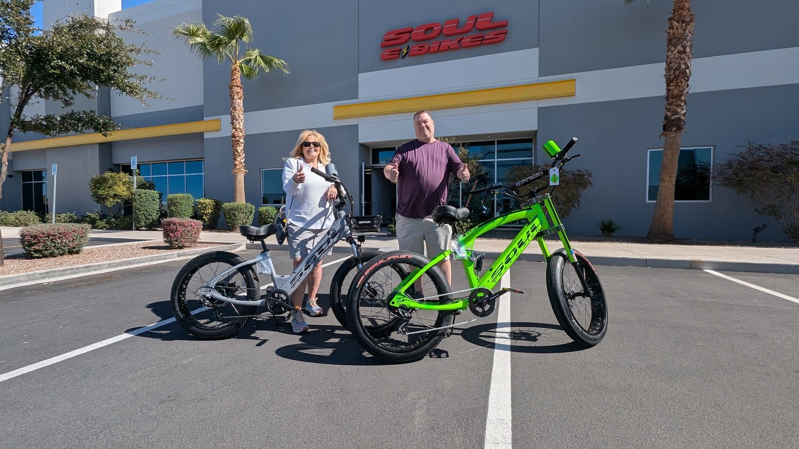 Two people posing with bicycles outside store.