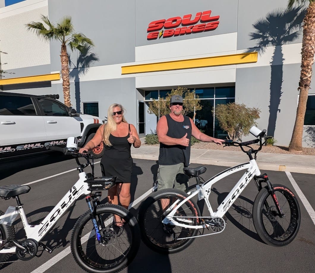 Two people with electric bikes outside store.