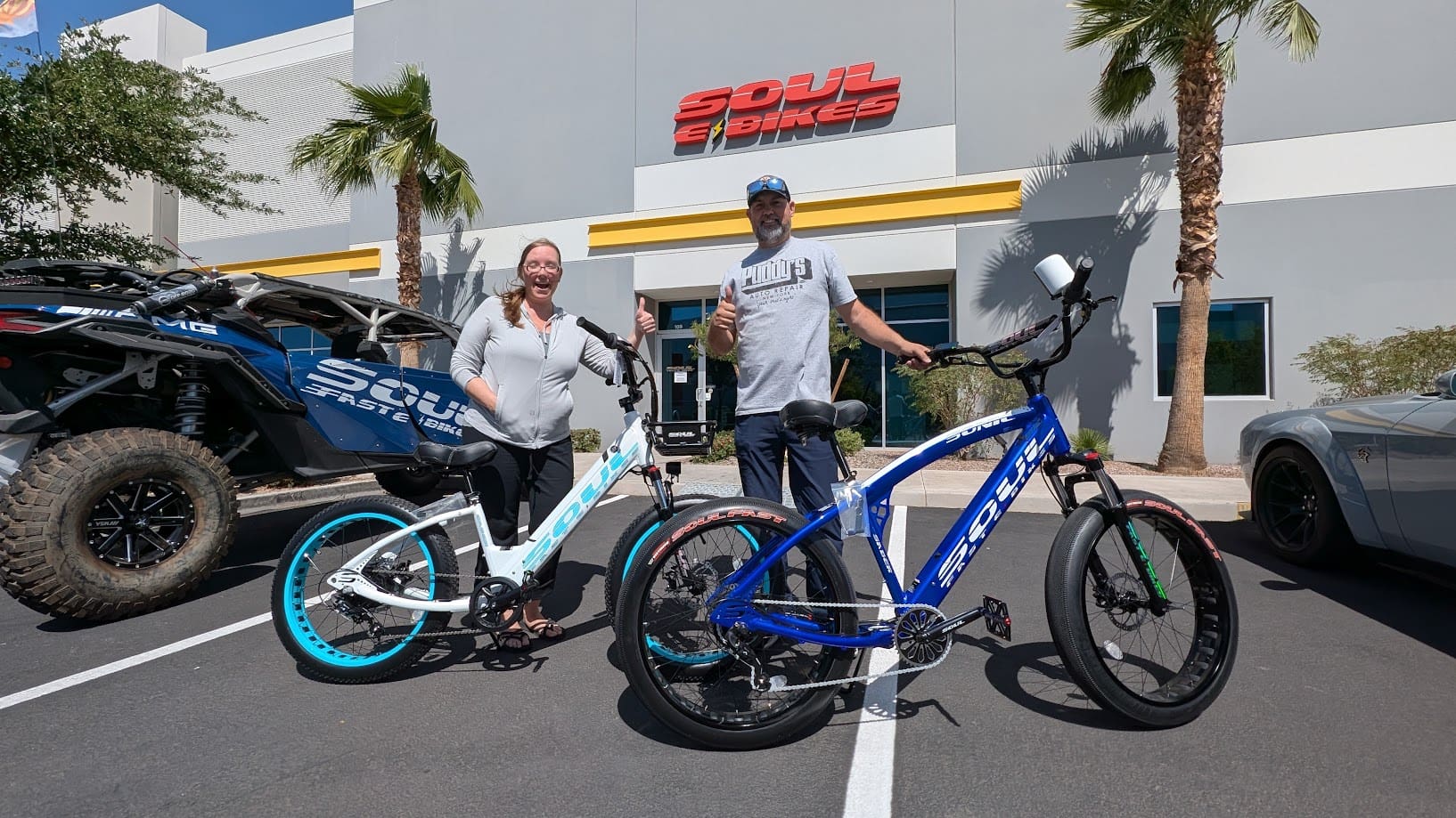 Two people with electric bikes outside shop.
