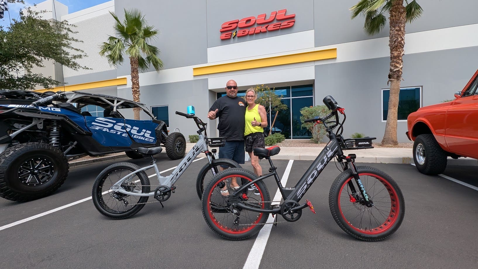 Couple posing with electric bikes outside store.
