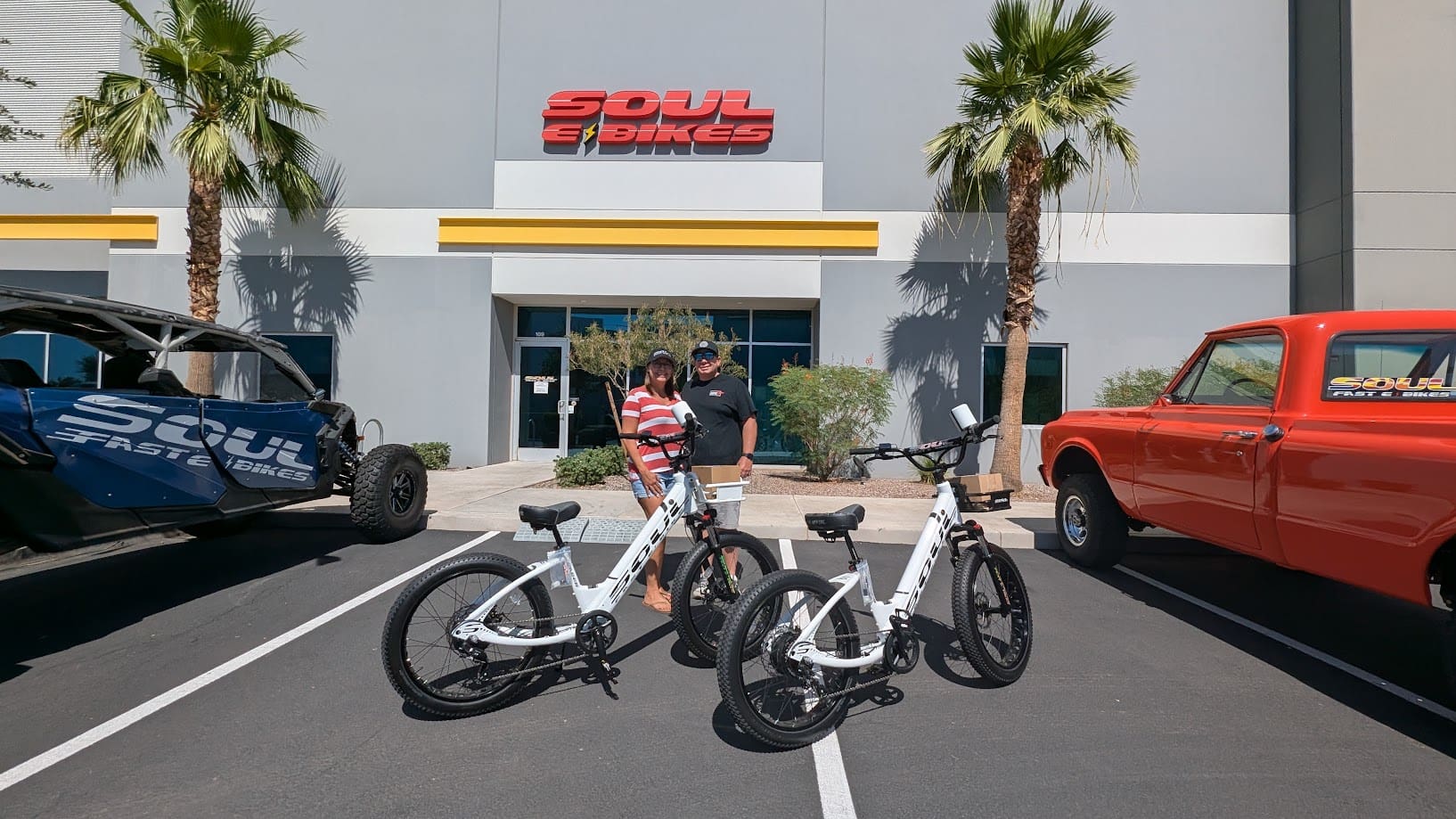 Two people with electric bikes outside store.