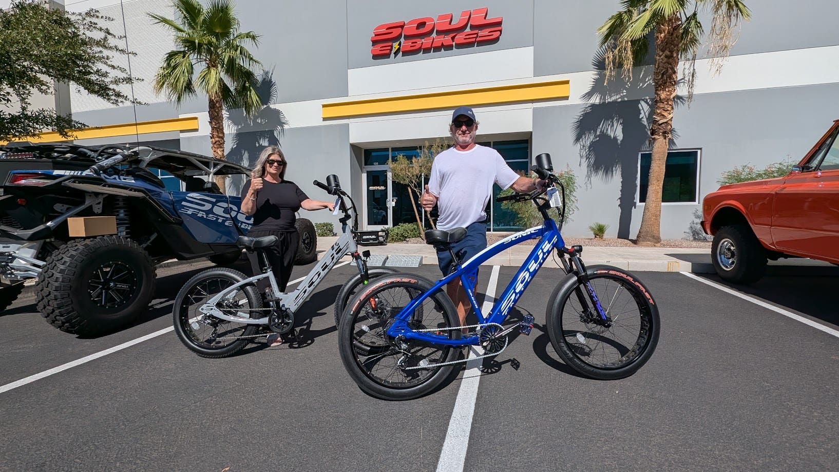 Two people posing with electric bicycles outside.