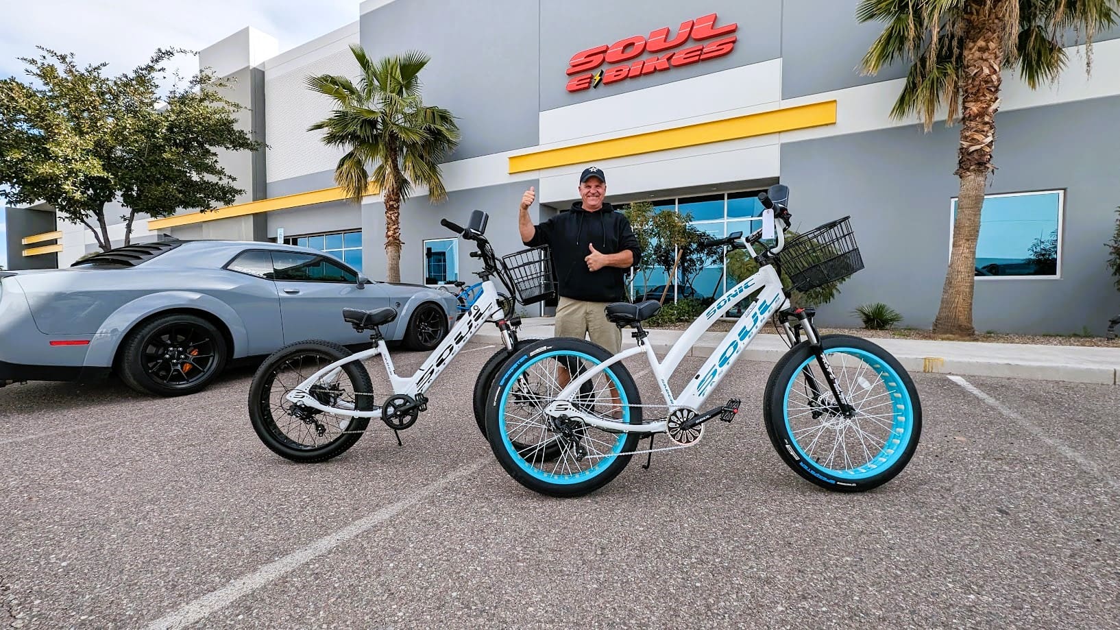 Man with two electric bikes outside store.
