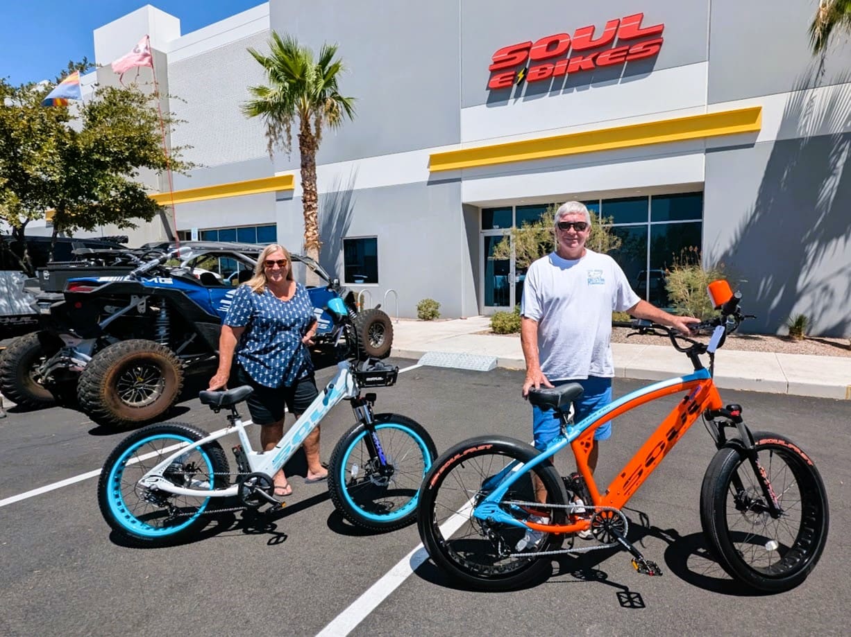 Two people with electric bikes outside store.