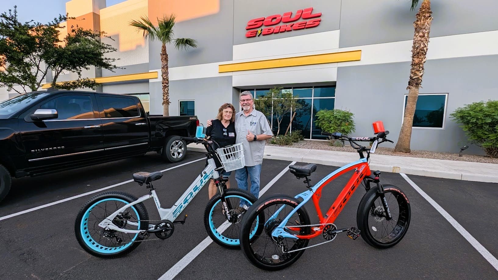 Two people with electric bikes outside store.