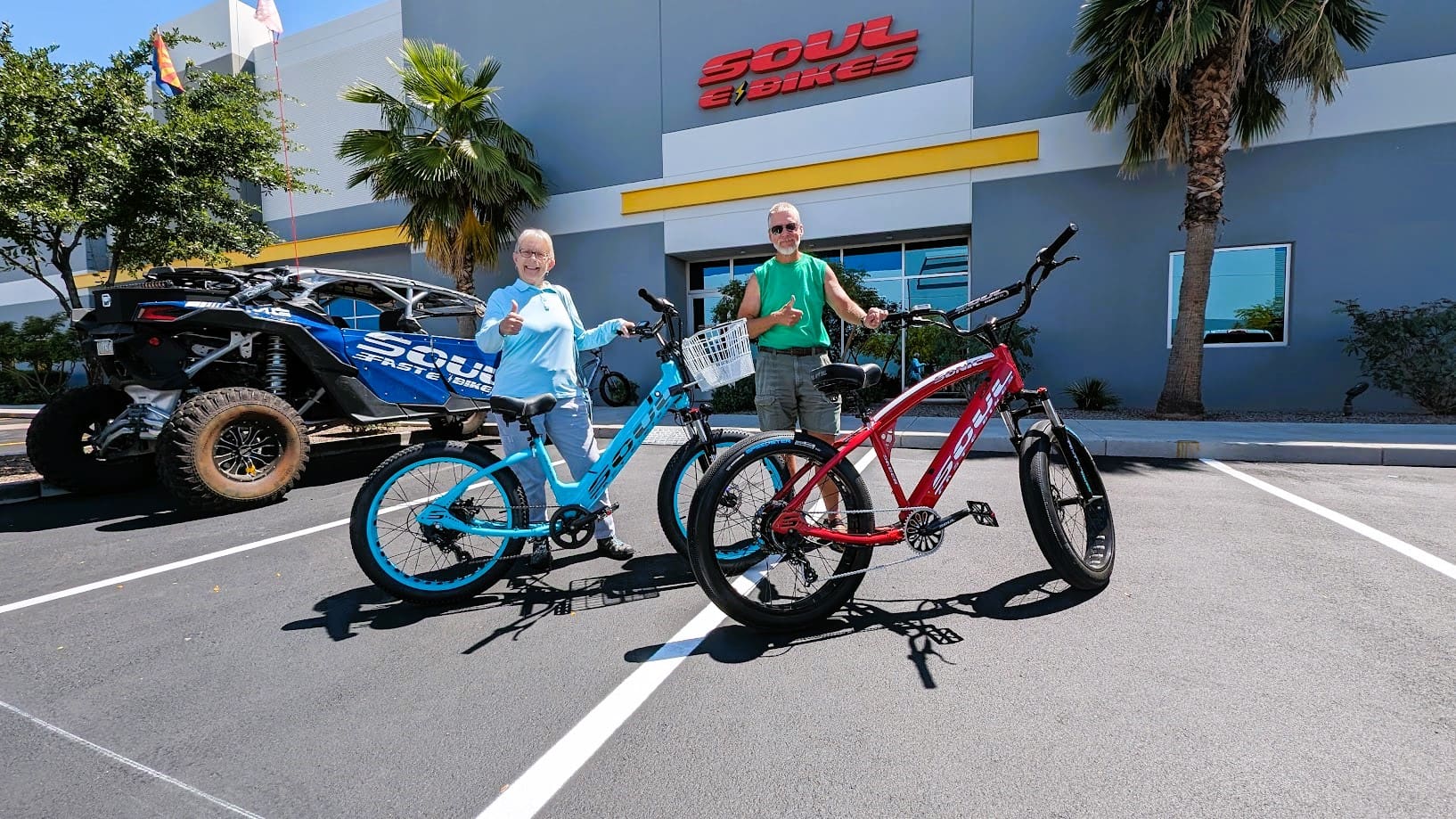 Two people posing with colorful bicycles outside.