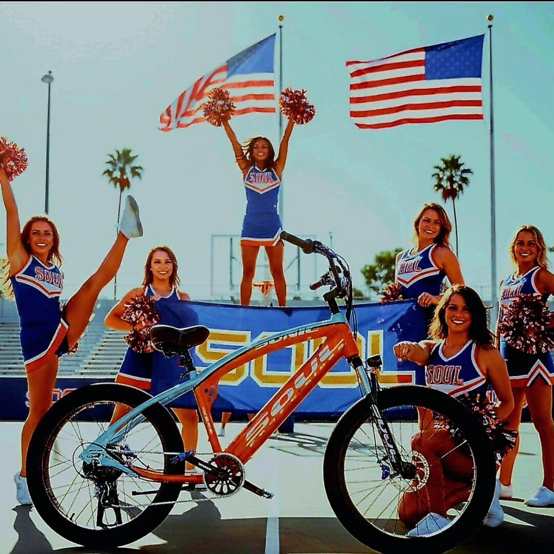 Cheerleaders posing with bicycle and flags.