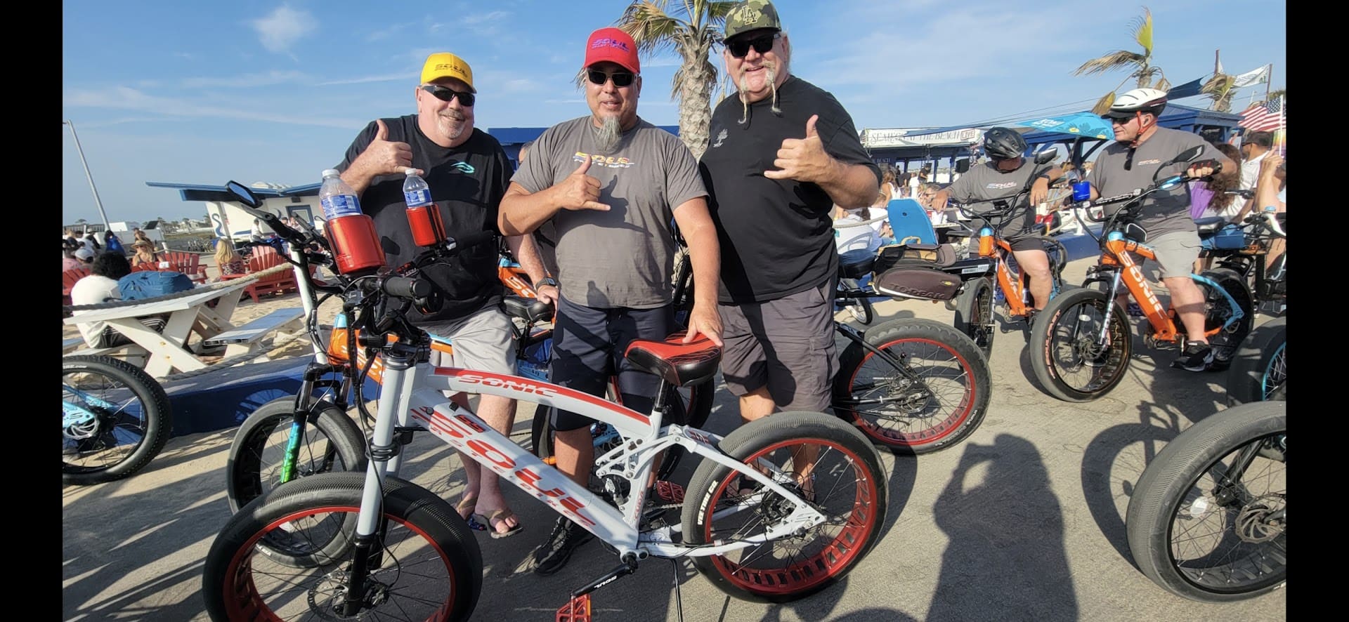 Three men posing with electric bikes outdoors.