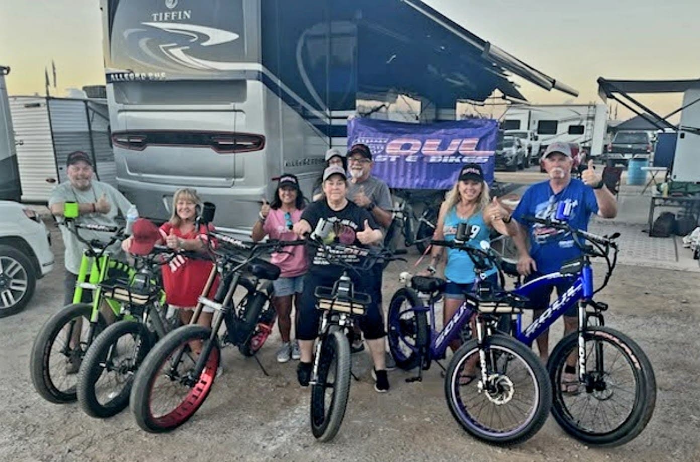 Group posing with electric bikes at campsite.