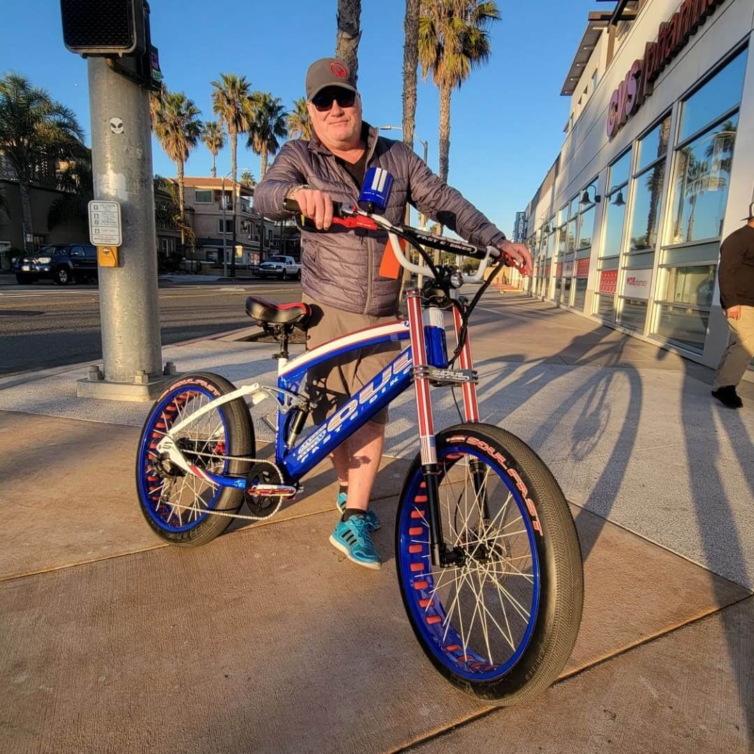 Man posing with a blue bicycle outdoors.