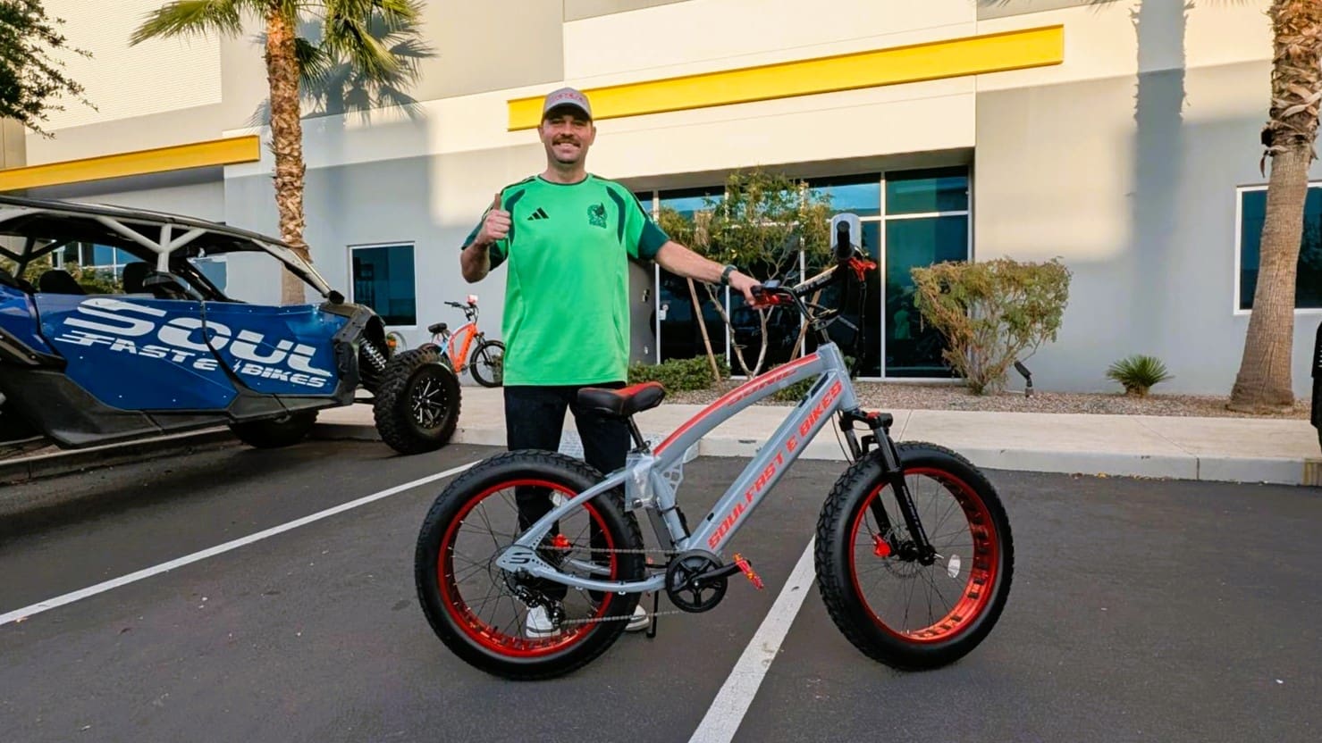Man posing with electric bicycle in parking lot.