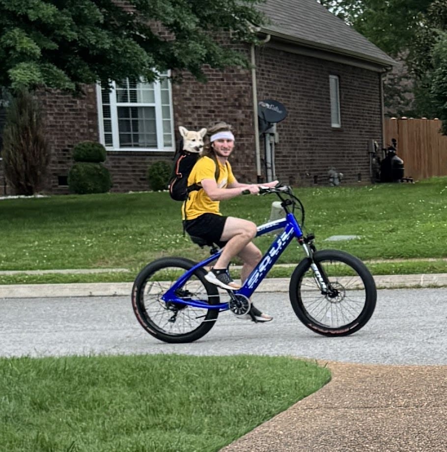 Man biking with dog in backpack.