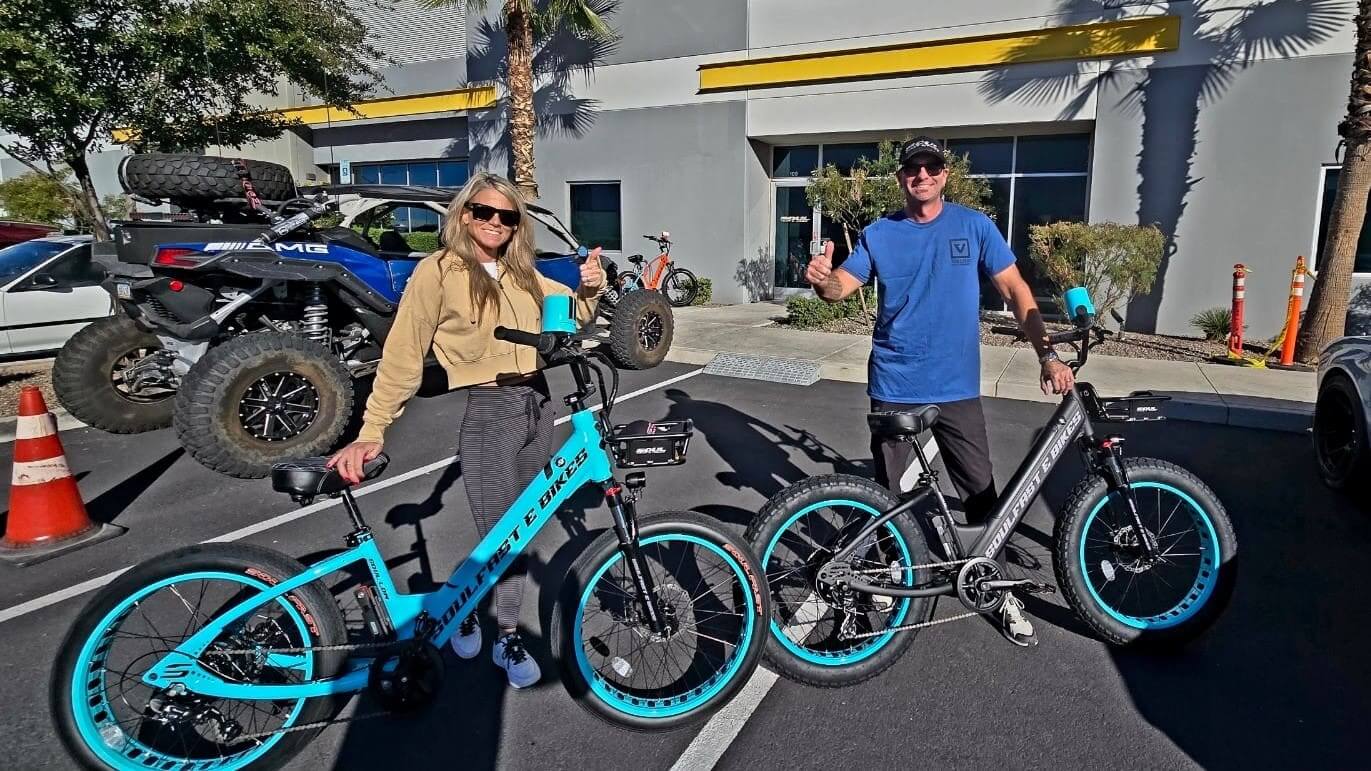 Two people with electric bikes outside building.